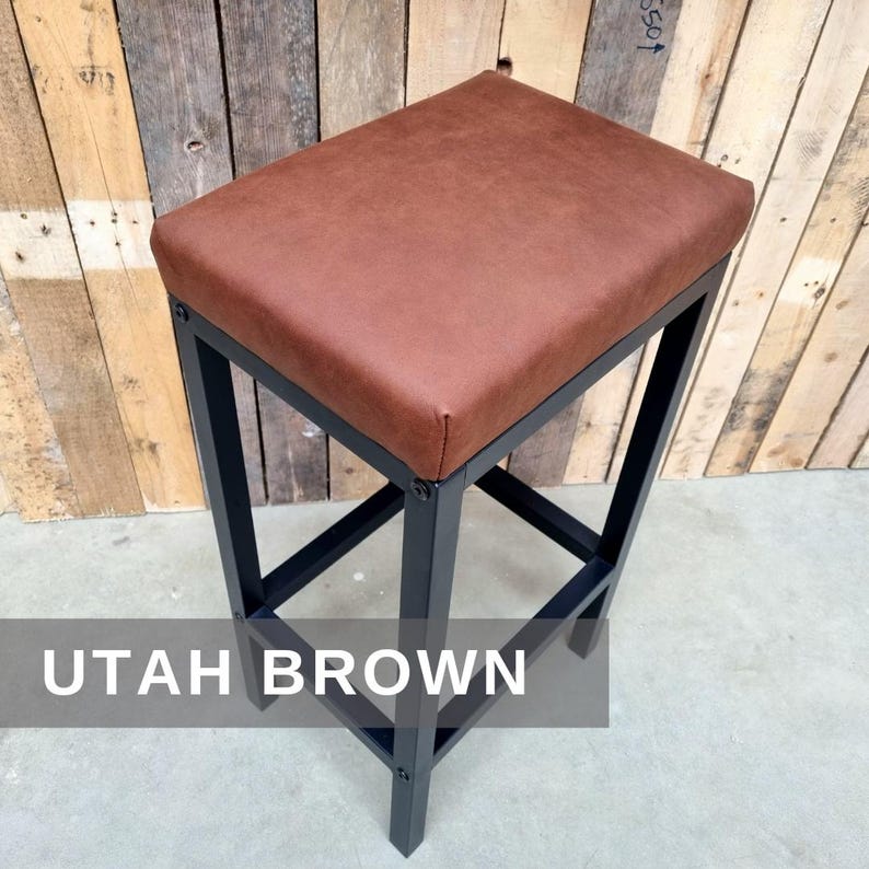 May include: A brown leather bar stool with a black metal frame. The stool has a square seat and a simple design. The text "UTAH BROWN" is visible in the image.