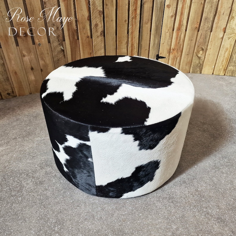 May include: Black and white cowhide ottoman with a round top. The ottoman is made of real cowhide and has a unique pattern.