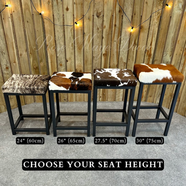 May include: Four black metal bar stools with different seat heights: 24 inches, 26 inches, 27.5 inches, and 30 inches. Each stool has a brown and white cowhide seat. The stools are lined up in order of height, with the shortest stool on the left and the tallest stool on the right. The text "CHOOSE YOUR SEAT HEIGHT" is printed below the stools.