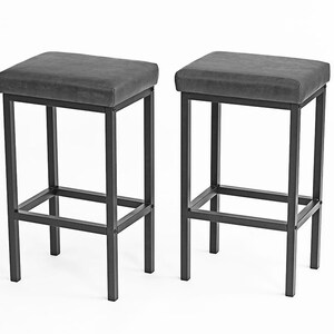 May include: Two black metal bar stools with gray upholstered seats. The stools have a simple, modern design and are perfect for a kitchen island or bar.