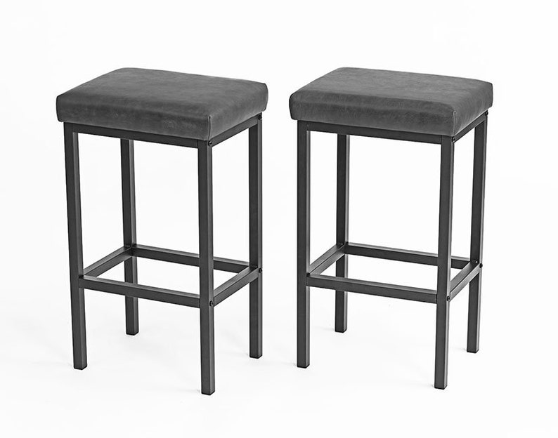 May include: Two black metal bar stools with gray upholstered seats. The stools have a simple, modern design and are perfect for a kitchen island or bar.