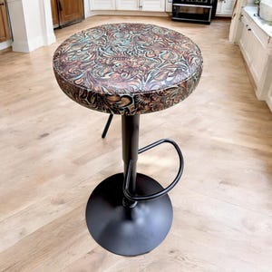 May include: A black swivel bar stool with a round, brown and teal patterned seat. The stool has a footrest.