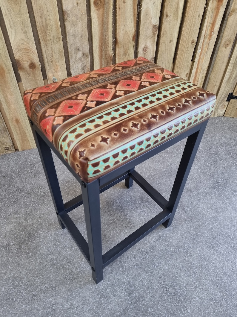 May include: A black metal bar stool with a colourful patterned leather seat. The seat features a geometric design with shades of brown, red, and turquoise.