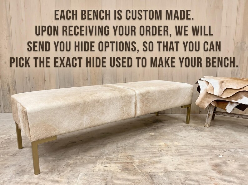 May include: A rectangular bench upholstered in light beige cowhide with a smooth texture, supported by four metallic gold-toned legs. The text reads: EACH BENCH IS CUSTOM MADE. UPON RECEIVING YOUR ORDER, WE WILL SEND YOU HIDE OPTIONS.