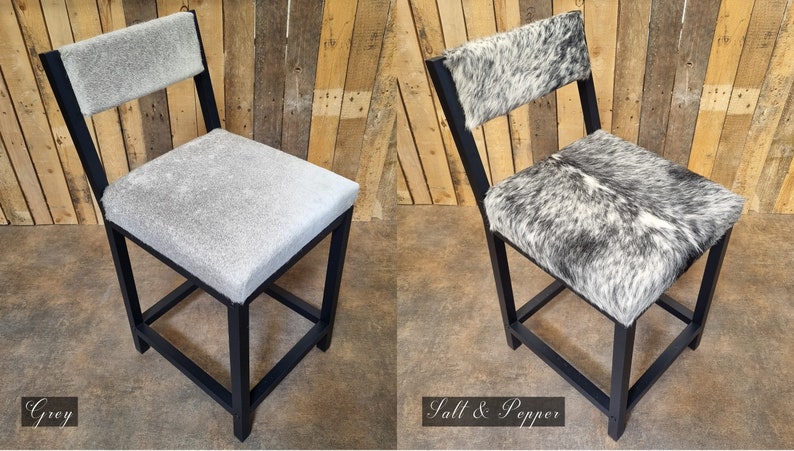 May include: Two black metal bar stools with a square base. The stool on the left has a gray cowhide seat and back. The stool on the right has a black and white cowhide seat and back. The stools are labeled "Grey" and "Salt & Pepper".