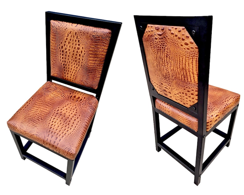 May include: Two black metal dining chairs with brown crocodile-embossed leather upholstery. The chairs have a square back and a simple, sturdy design.