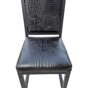 May include: Black bar stool with a crocodile-embossed leather seat and backrest. The stool has a square frame and a simple design.