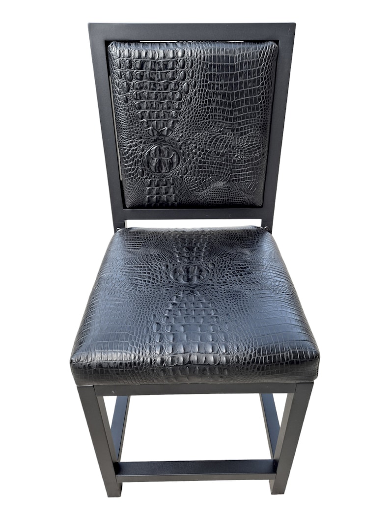 May include: Black bar stool with a crocodile-embossed leather seat and backrest. The stool has a square frame and a simple design.