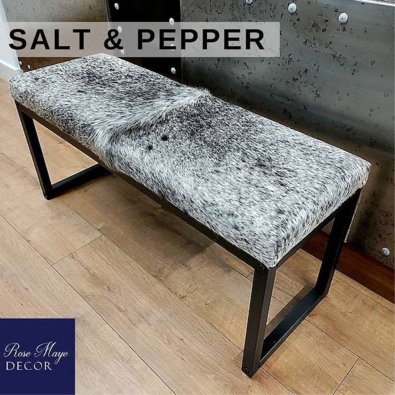 May include: A black metal bench with a white and black cowhide seat. The bench is labelled "SALT & PEPPER".