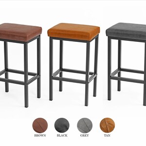 May include: Three bar stools with black metal frames and upholstered seats. The stools are available in brown, black, and gray.