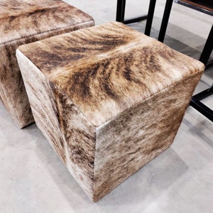Pu&ograve; includere: Due pouf quadrati in pelle di mucca marrone e bianca. I pouf sono realizzati in un materiale morbido e soffice e hanno un motivo naturale unico.