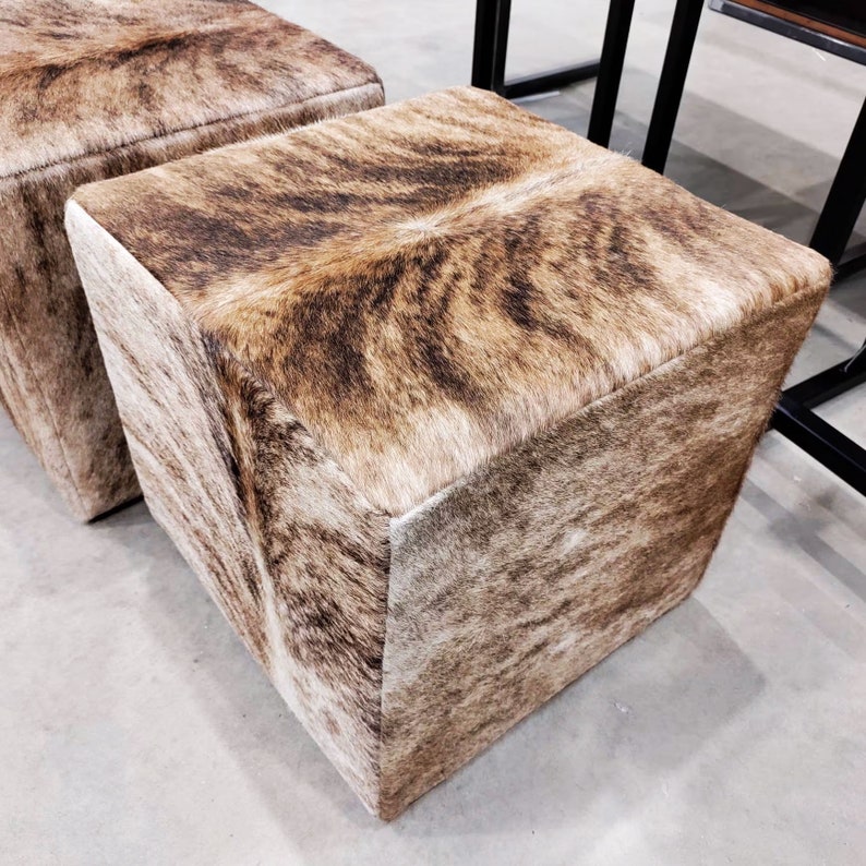 Pu&ograve; includere: Due pouf quadrati in pelle di mucca marrone e bianca. I pouf sono realizzati in un materiale morbido e soffice e hanno un motivo naturale unico.