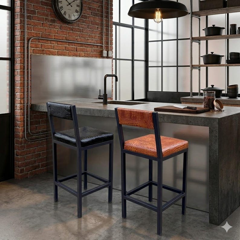 May include: Two black metal bar stools with textured seat and backrests. One stool has a black seat and back, the other has a brown seat and back. The stools are in a kitchen setting with a brick wall and stainless steel accents.