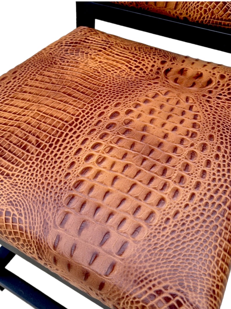 May include: A brown leather chair with a crocodile-embossed pattern on the seat. The chair has a black metal frame.