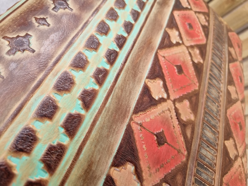 May include: Close-up of a brown leather surface with a turquoise and red geometric pattern. The pattern is embossed into the leather and has a distressed look.