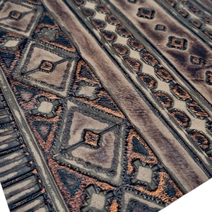May include: Close-up of a brown leather fabric with a geometric pattern embossed in copper. The pattern is a series of repeating diamonds and triangles.