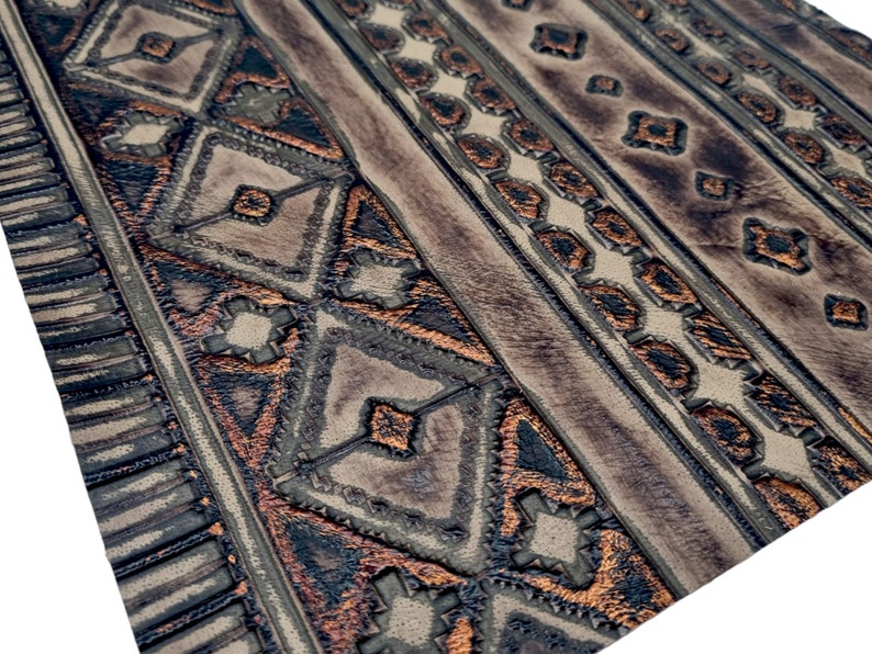 May include: Close-up of a brown leather fabric with a geometric pattern embossed in copper. The pattern is a series of repeating diamonds and triangles.