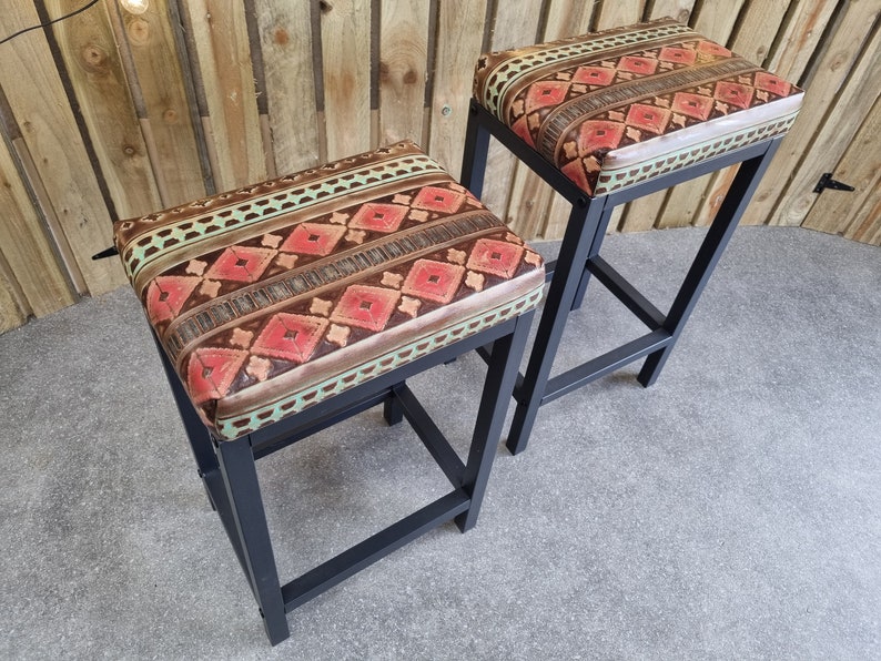May include: Two black metal bar stools with a geometric patterned fabric seat in shades of brown, red, and green.