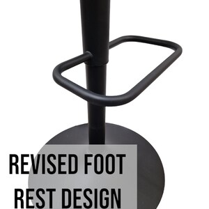 May include: Black metal bar stool with a footrest and a round base. The footrest has a revised design. The text "REVISED FOOT REST DESIGN" is printed on the base.