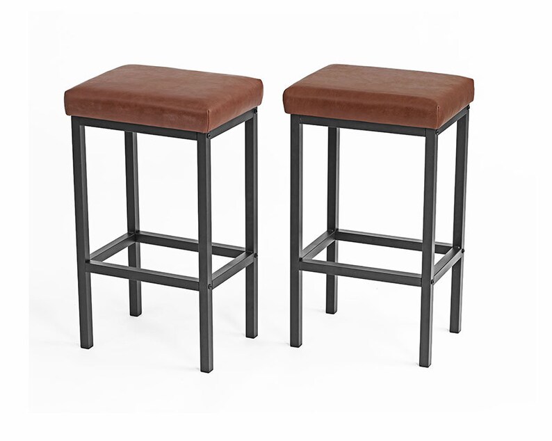 May include: Two brown leather bar stools with black metal frames. The stools have a simple design with a rectangular seat and a single crossbar for support.