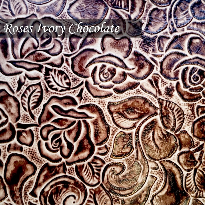 Op de afbeelding: Close-up van een bruin lederen oppervlak met een herhalend patroon van ge&euml;mbosseerde rozen. Het leer heeft een licht ivoorachtige achtergrond met bruine rozen. De tekst "Roses Ivory Chocolate" is zichtbaar bovenaan de afbeelding.