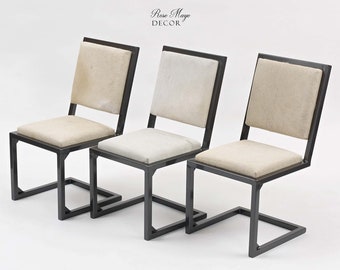Puede incluir: Tres sillas de metal negro con asientos y respaldos de tela beige. Las sillas tienen un diseño simple y moderno con un marco cuadrado y una base curva.