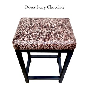 Op de afbeelding: Een zwarte metalen barstoel met een bruine en ivoren leren zitting met een rozenpatroon. De tekst "Roses Ivory Chocolate" staat boven de stoel.