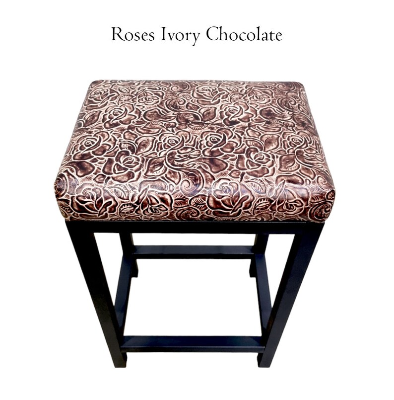 Op de afbeelding: Een zwarte metalen barstoel met een bruine en ivoren leren zitting met een rozenpatroon. De tekst "Roses Ivory Chocolate" staat boven de stoel.