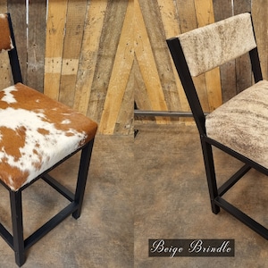May include: Two black metal bar stools with cowhide upholstery. The stool on the left has a tan and white cowhide pattern. The stool on the right has a beige brindle cowhide pattern.