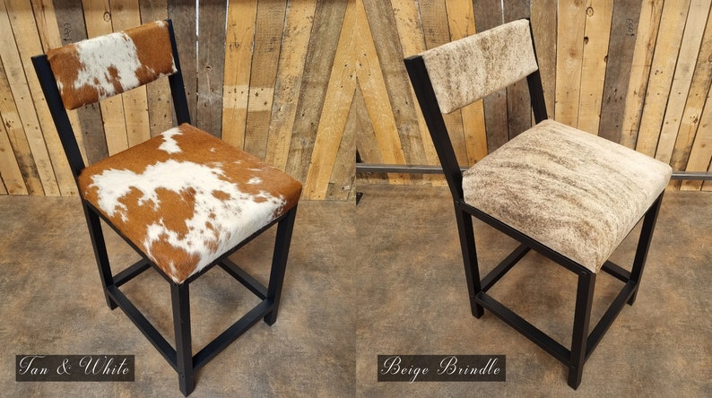 May include: Two black metal bar stools with cowhide upholstery. The stool on the left has a tan and white cowhide pattern. The stool on the right has a beige brindle cowhide pattern.