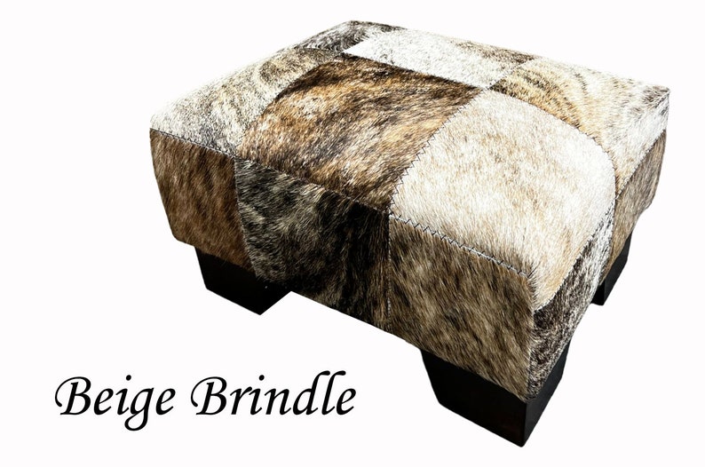 May include: Beige and brown patchwork cowhide ottoman with black wooden legs.