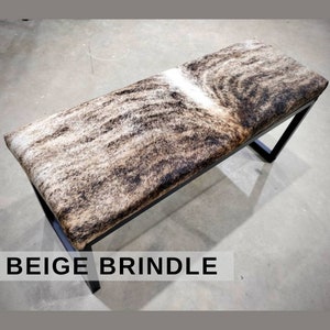 May include: A beige and brown cowhide bench with a black metal frame. The bench has a natural, rustic look and is perfect for adding a touch of western style to any room.