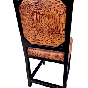 May include: A black metal bar stool with a brown crocodile-embossed leather seat and back. The stool has a square base and a rectangular back.