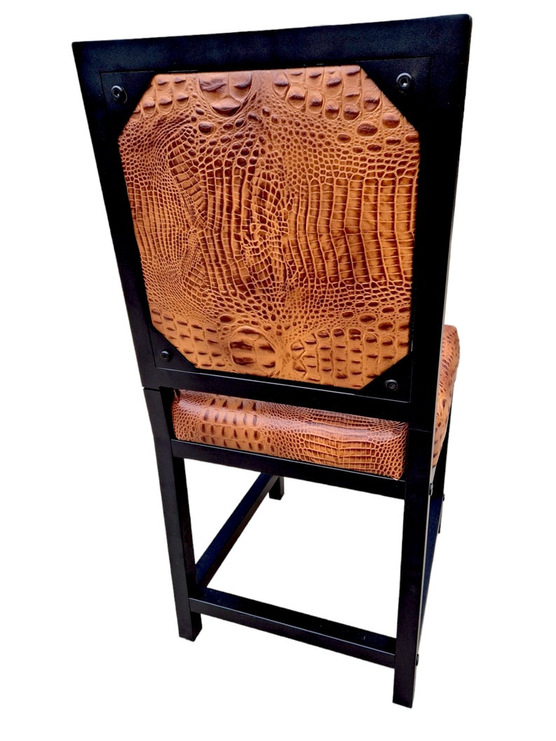 May include: A black metal bar stool with a brown crocodile-embossed leather seat and back. The stool has a square base and a rectangular back.