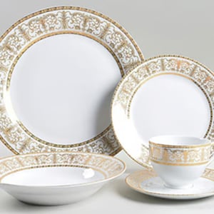 May include: A white porcelain dinnerware set with gold filigree and trim. The set includes a large dinner plate, a smaller plate, a bowl, a teacup, and a saucer. The gold design is ornate and detailed, creating an elegant aesthetic.