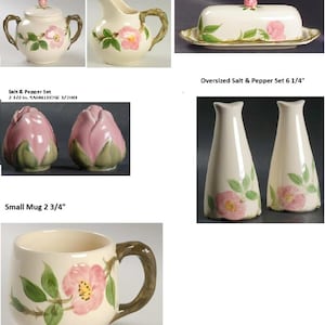 May include: A collection of cream-colored ceramic tableware featuring a floral design with pink roses and green leaves. The set includes a sugar bowl with lid, creamer, butter dish, salt and pepper shakers, and a small mug. The butter dish measures 7.75 inches long.