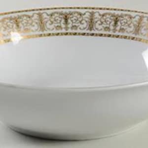 May include: White ceramic serving bowl with a gold decorative border. The gold border features an ornate, repeating pattern. The bowl has a simple, elegant design, suitable for serving various dishes. The bowl is likely part of a dinnerware set.