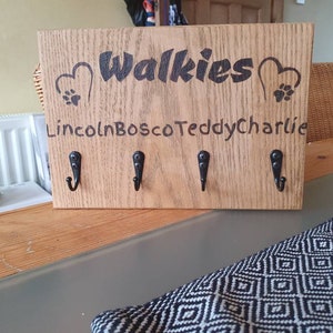 Puede incluir: Porta llaves de madera con cuatro ganchos y el texto "Walkies" con huellas de patas y corazones. Los nombres "Lincoln, Bosco, Teddy, Charlie" están escritos debajo del texto.