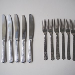 Puede incluir: Un juego de ocho cubiertos plateados, que incluye siete cuchillos y un tenedor. Los cubiertos tienen un patrón decorativo en los mangos.