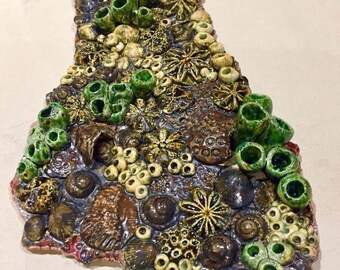 以下が含まれることがあります： 貝殻、ヒトデ、サンゴなど、さまざまな海洋生物を描いたセラミック製の壁飾り。彫刻は茶色、緑色、白色でできています。