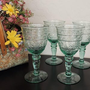 May include: Four clear green glass wine glasses with an etched design. The glasses are on a dark surface.