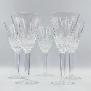 May include: Five clear crystal wine glasses. The glasses have a diamond-cut pattern on the bowl and a faceted stem. The glasses are arranged in a row, with the stems and bases visible.