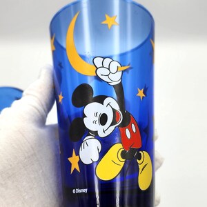 May include: Blue drinking glass featuring Mickey Mouse with a yellow crescent moon and stars. Mickey is wearing red shorts, yellow shoes, and white gloves. The Disney logo is at the bottom.