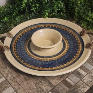 May include: A ceramic serving dish with a smaller bowl in the center. The dish has a blue and brown patterned design with two handles on the sides.