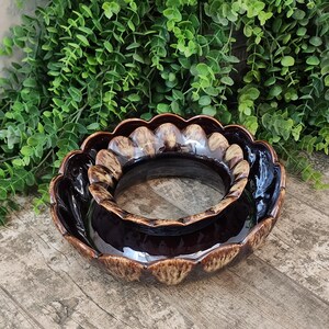 May include: Two brown ceramic bowls with scalloped edges. The bowls are nested, with a glossy dark brown interior and a lighter, textured rim. The bowls are likely for decorative or functional use.