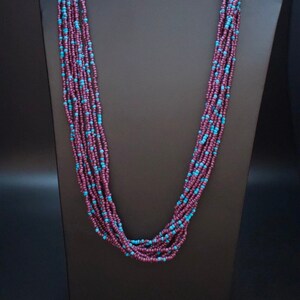 May include: A long multi-strand necklace made of small purple and turquoise beads. The necklace is displayed on a black mannequin.