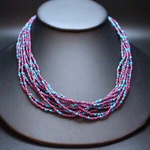 May include: A multi-strand necklace made of small, dark purple and turquoise beads. The necklace is layered and has a simple, elegant design.