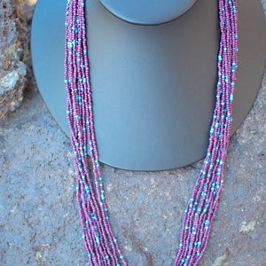 May include: A multi-strand necklace made of small purple and blue beads. The necklace is displayed on a black mannequin bust.
