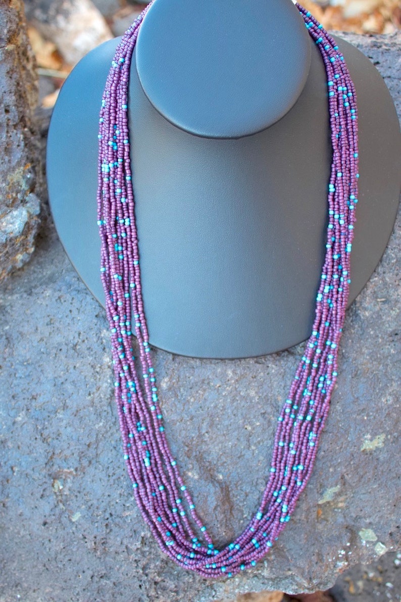 May include: A multi-strand necklace made of small purple and blue beads. The necklace is displayed on a black mannequin bust.