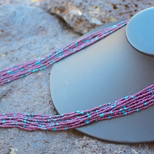May include: A multi-strand necklace made of small purple and turquoise beads. The necklace is displayed on a black mannequin bust.